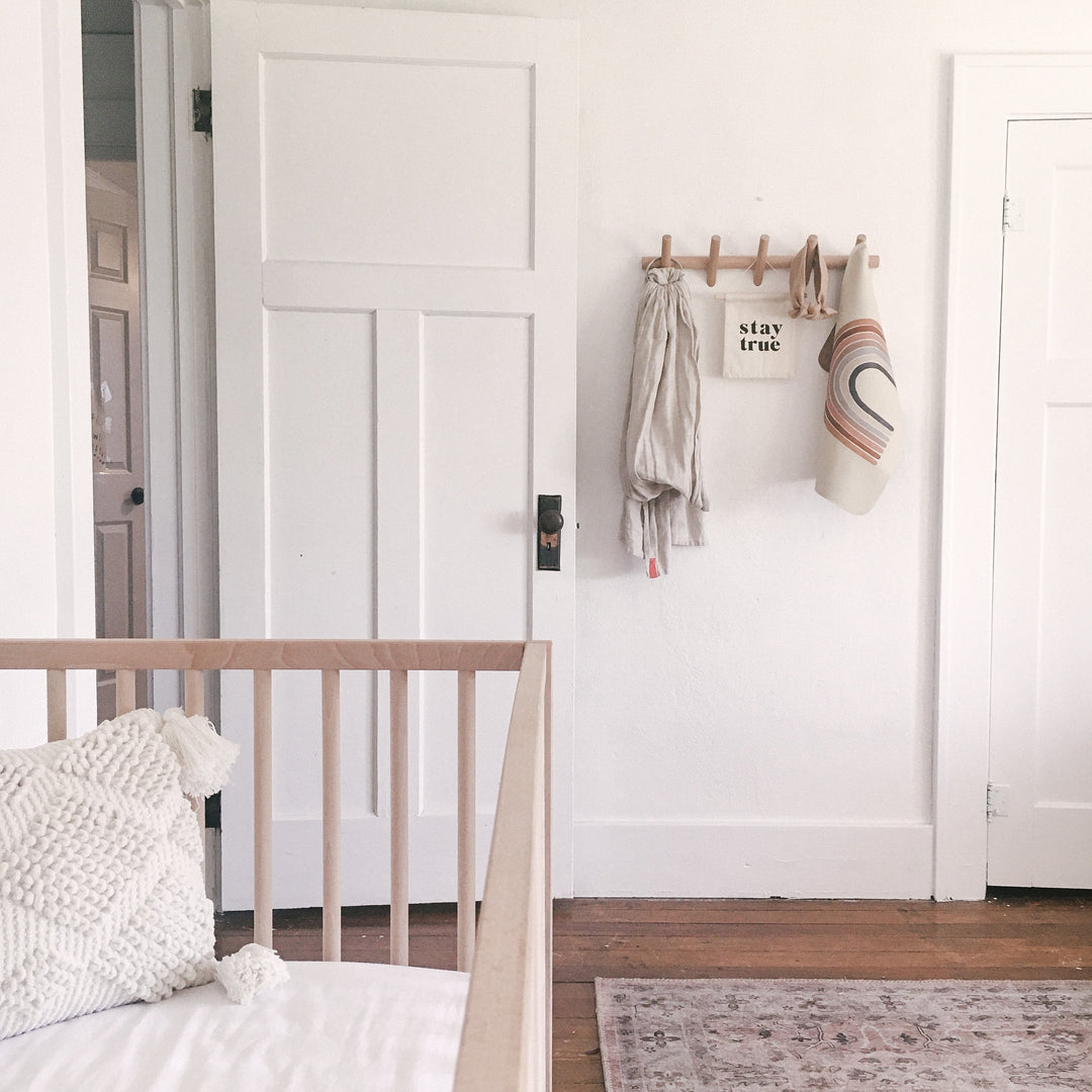 Beechwood wall coat rack with 5 hooks, featuring a minimalist design, holding a linen scarf and a rainbow-striped towel.