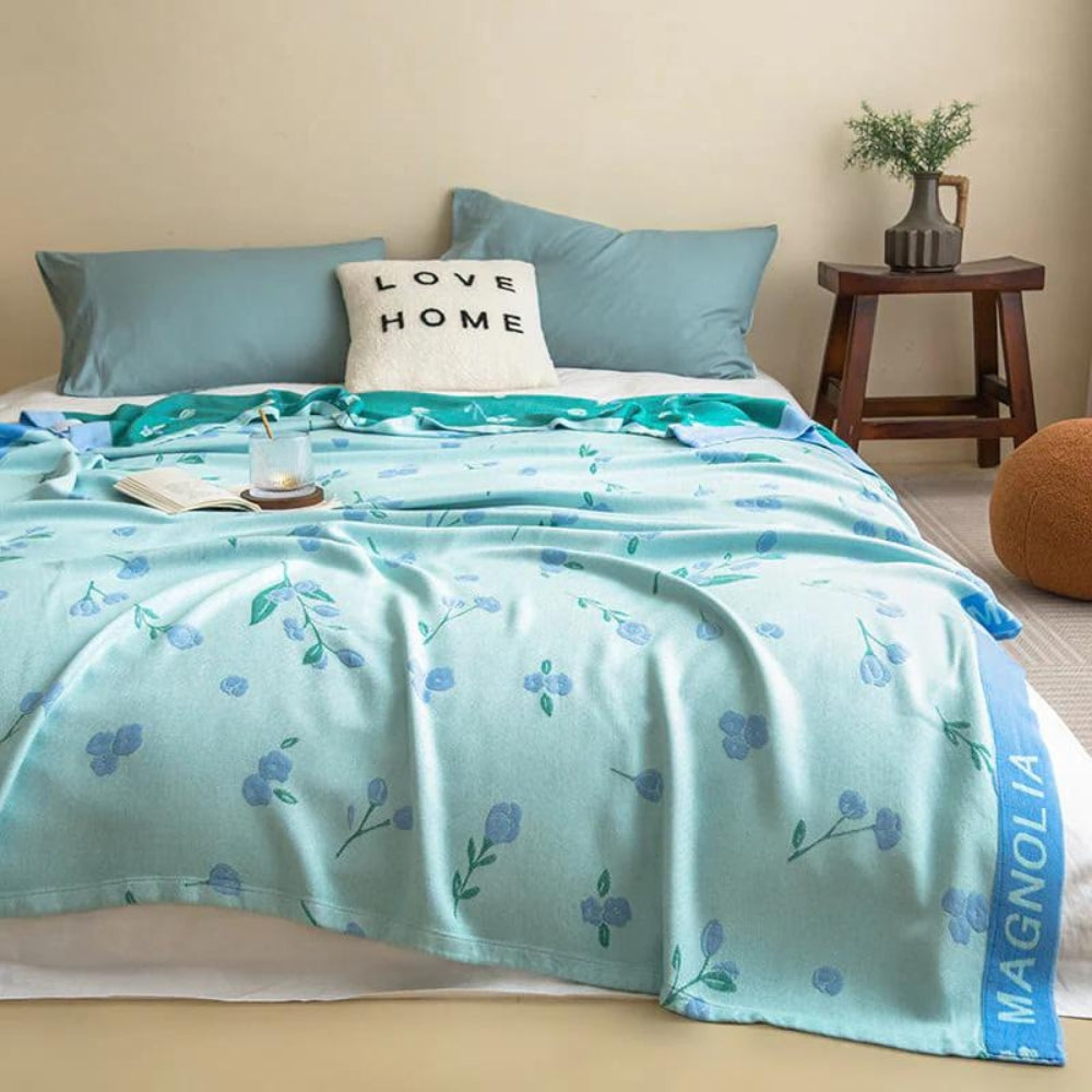 Blue floral bamboo cooling blanket draped on a bed with pillows and a book.