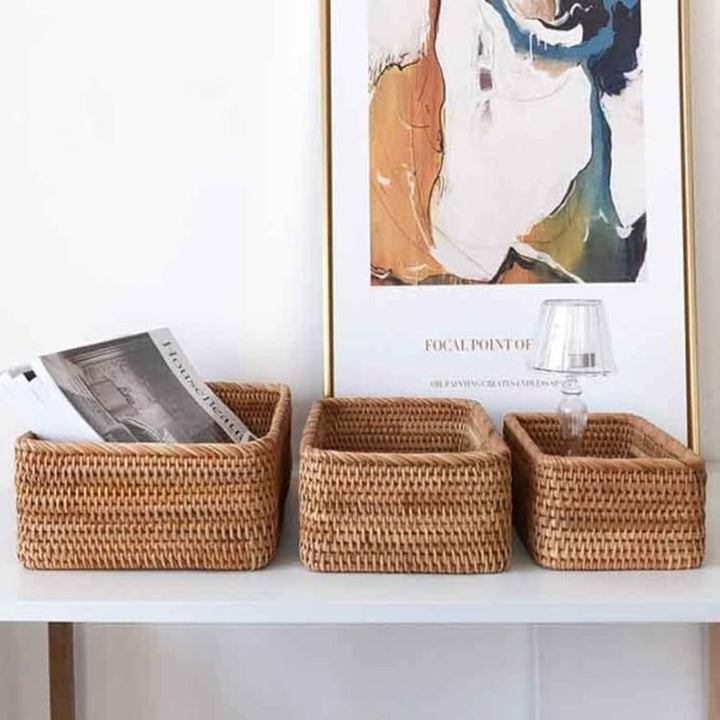 Three hand-woven rattan storage baskets on a white shelf, one holding magazines.