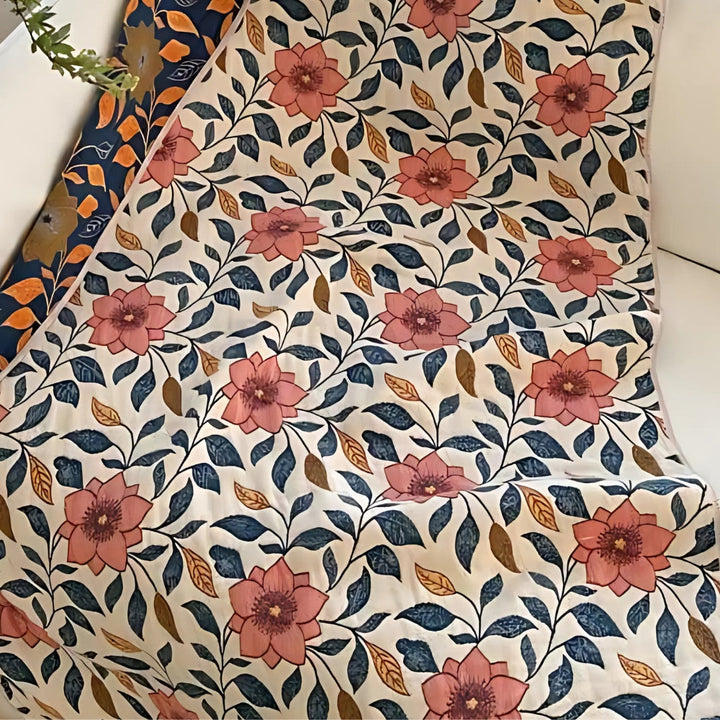 Cotton gauze bath towel with a repeating pattern of pink flowers and blue-green leaves on a cream background.