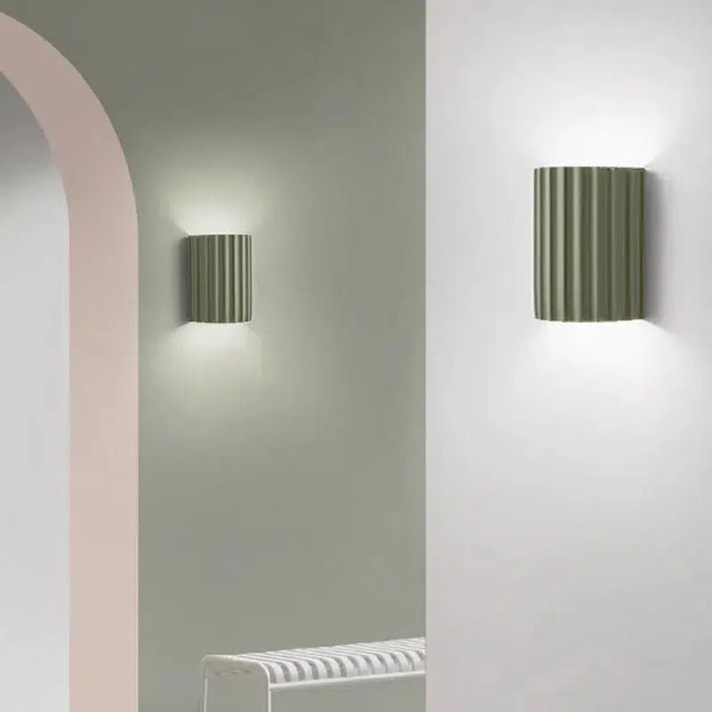 Two ribbed, olive green LED wall sconces mounted on a light green wall, casting a warm glow.