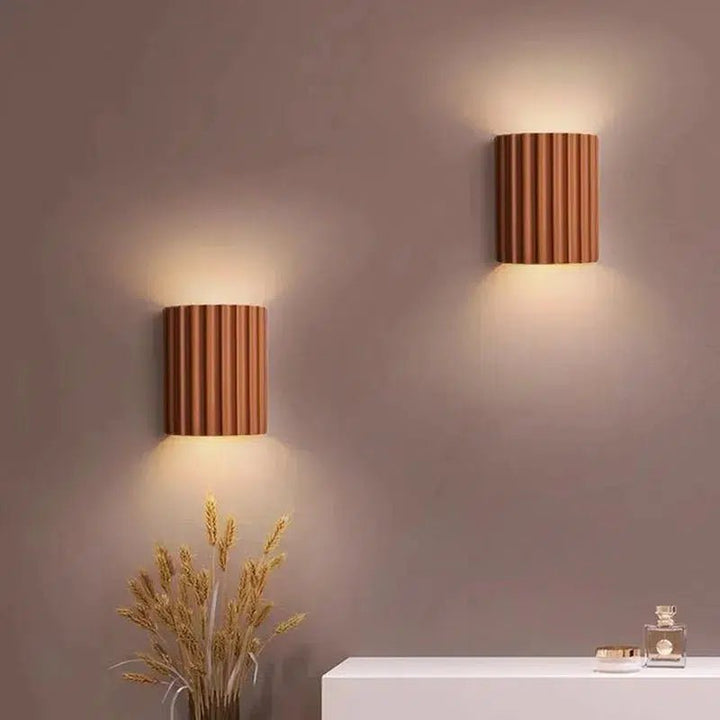 Two copper-colored fluted wall sconces mounted on a taupe wall, casting warm light downwards.