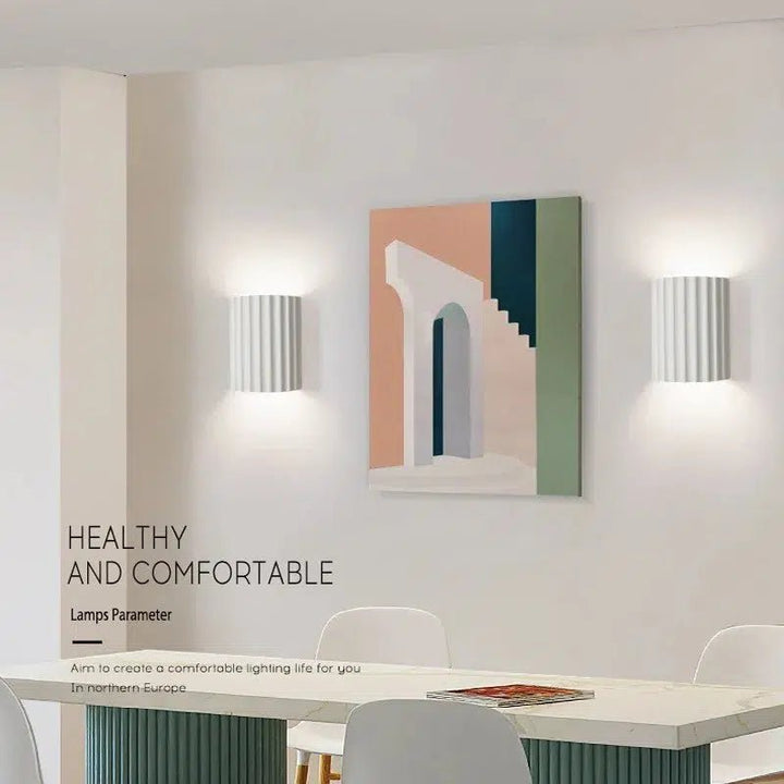 Two white fluted LED wall sconces flank a colorful abstract painting in a dining room.