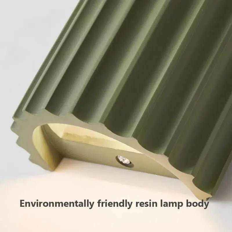 Green resin wall sconce with a fluted design and integrated LED light.