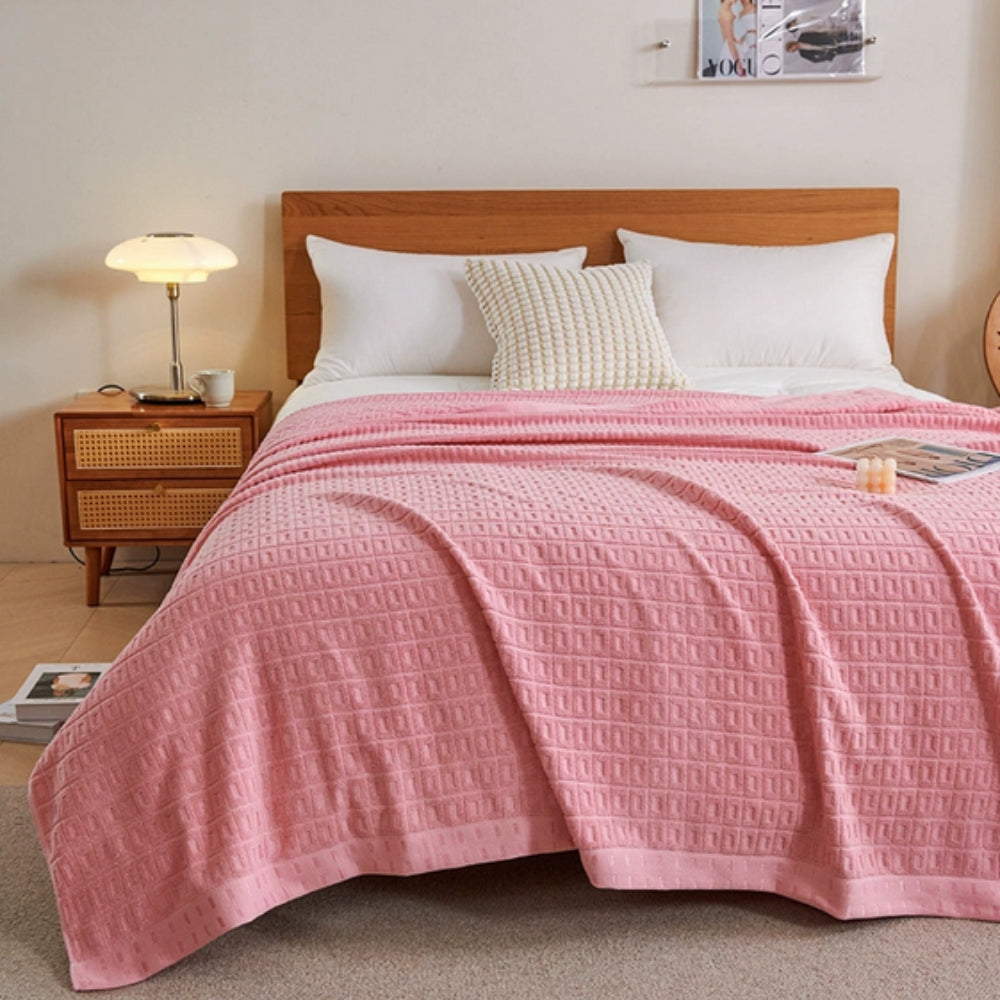Pink waffle weave cotton summer bedspread throw blanket draped on a bed.