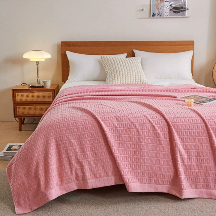 Pink waffle weave cotton summer bedspread throw blanket draped on a bed.