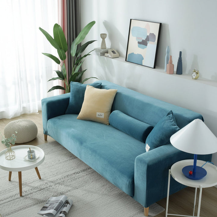 Lake blue velvet couch cover on a sofa with decorative pillows and a round side table.