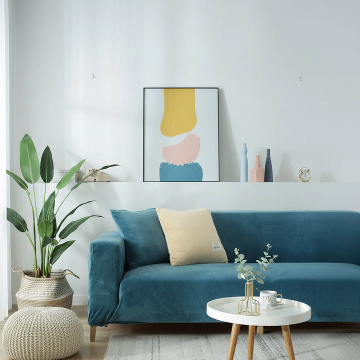 Lake blue velvet couch cover on a sofa with a yellow pillow and a small white table.