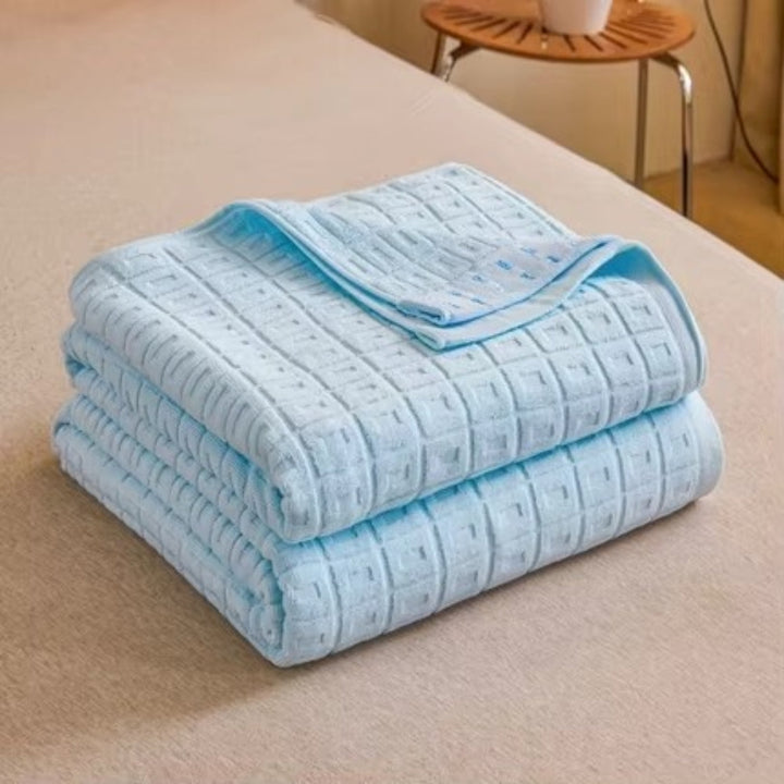 Two folded light blue waffle weave cotton blankets stacked on a bed.