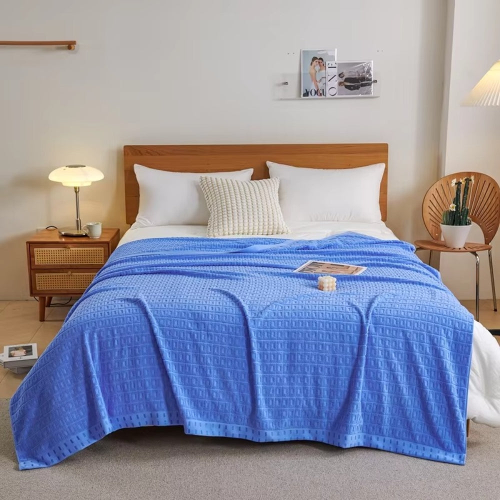 Blue waffle cotton summer bedspread throw blanket on a bed with white pillows and a wooden headboard.