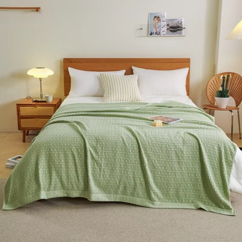 Sage green waffle cotton summer bedspread throw blanket draped on a bed with white pillows.