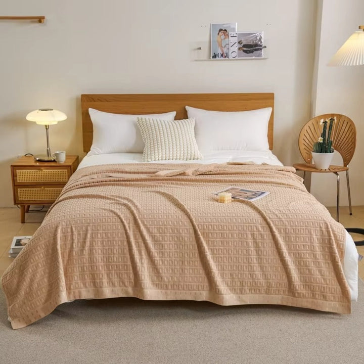 Beige waffle cotton summer bedspread throw blanket draped over a bed with white pillows.