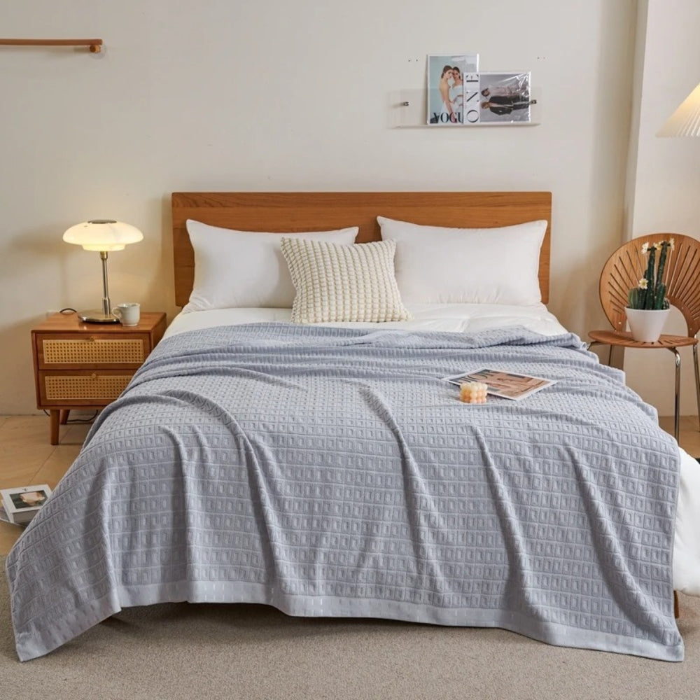Gray waffle cotton summer bedspread throw blanket draped over a bed with white pillows.