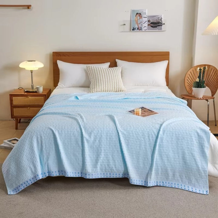 Light blue waffle cotton summer bedspread throw blanket draped on a bed with white pillows.