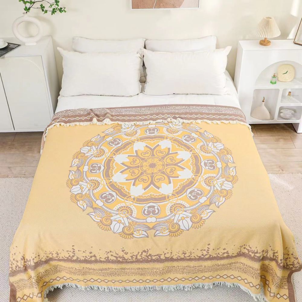 Yellow cotton boho mandala blanket with fringe on a bed with white pillows.