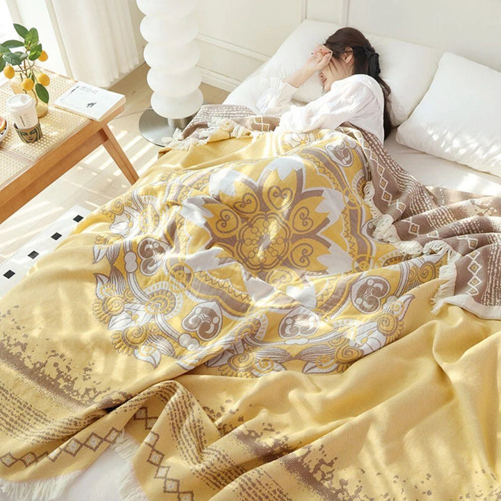 A woman sleeps under a yellow boho mandala cotton blanket with fringe.