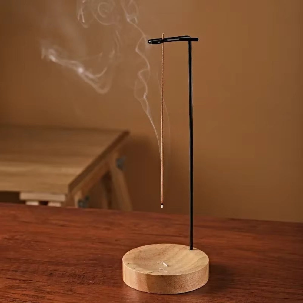 Minimalist wooden incense burner with a thin incense stick burning and smoke rising.