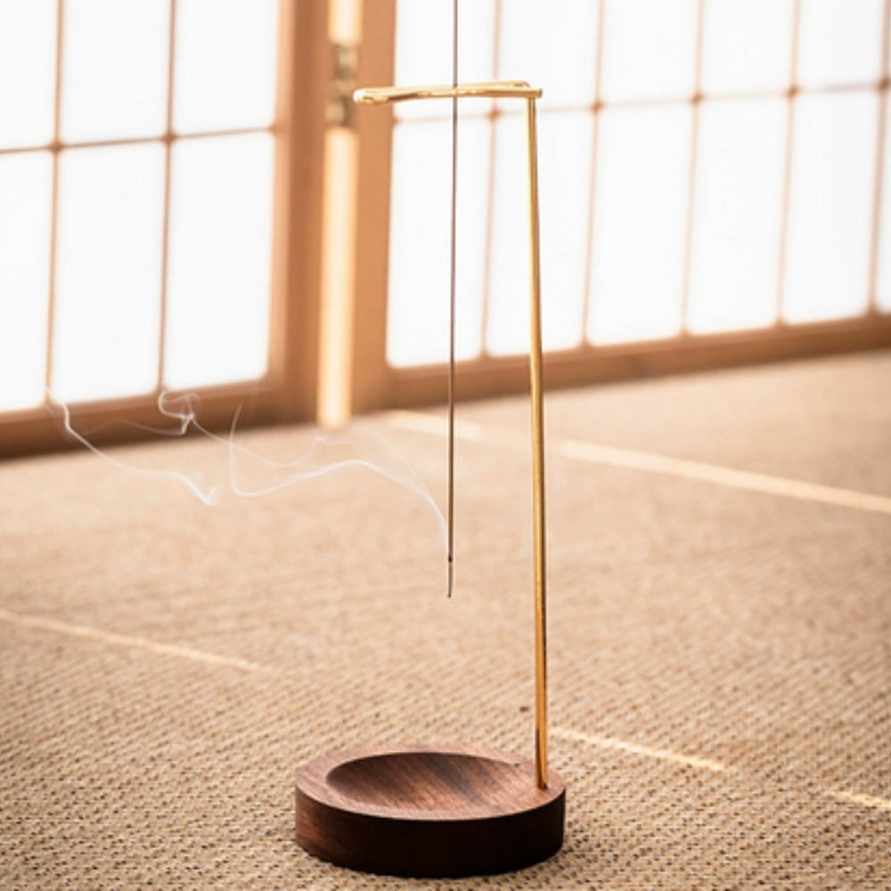 Minimalist wooden incense burner with a thin metal stand holding a lit incense stick, emitting smoke.
