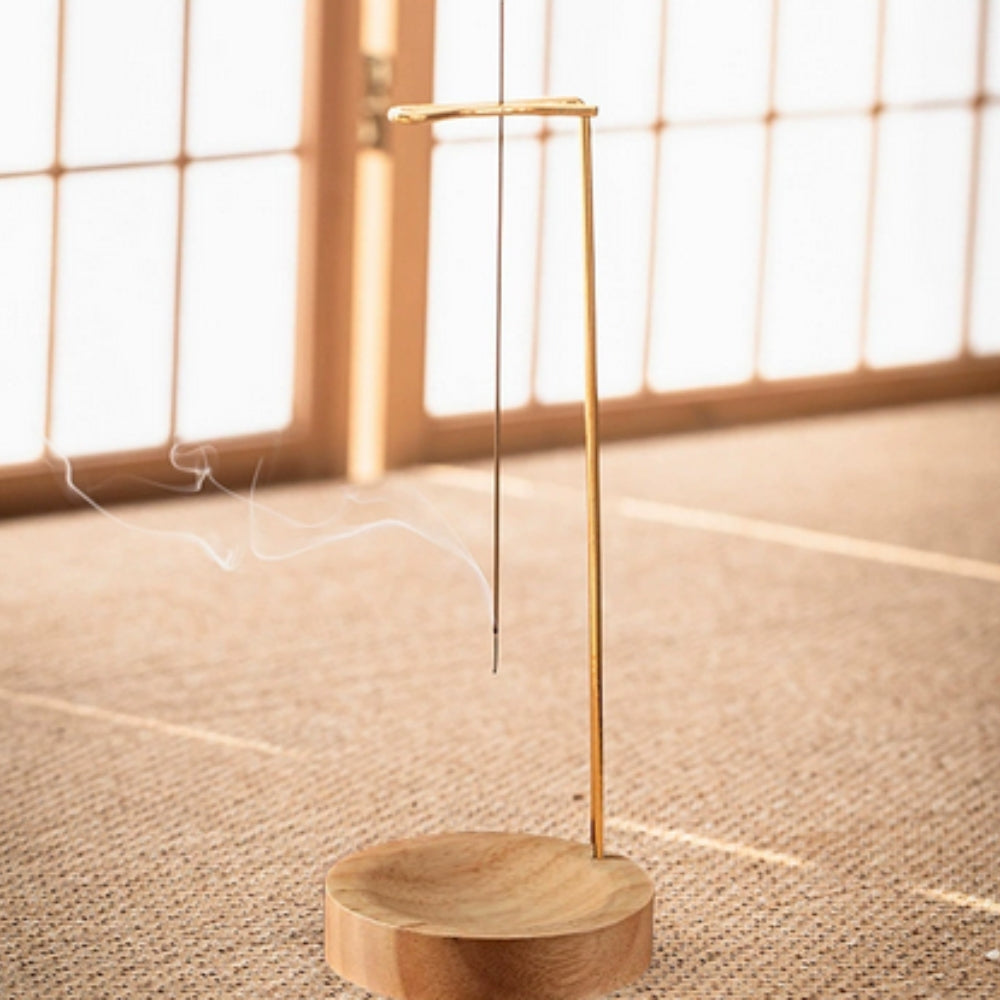 Minimalist wooden incense burner with a thin metal stand holding an incense stick, with smoke gently rising.