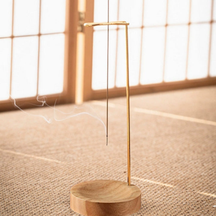 Minimalist wooden incense burner with a thin metal stand holding an incense stick, with smoke gently rising.