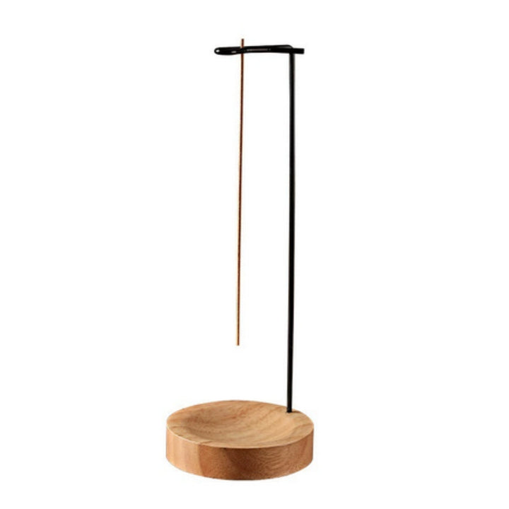 Minimalist incense burner with a round wooden base and a tall black metal stand holding an incense stick.