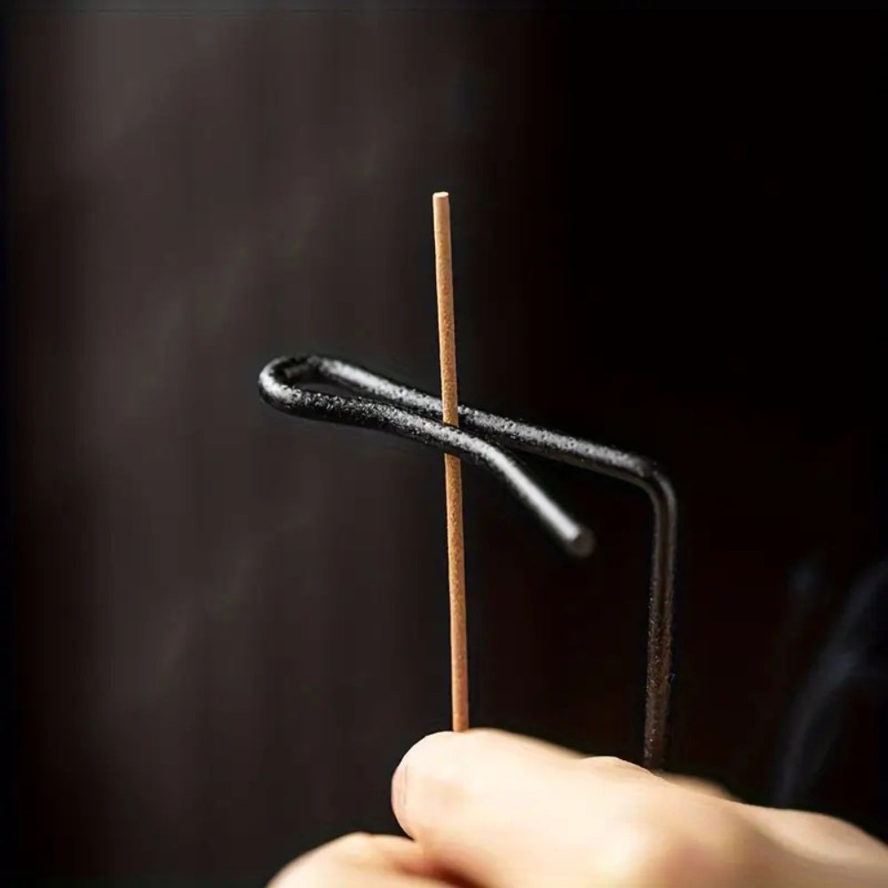 A hand holds a wooden incense stick with a metal holder, with smoke rising against a dark background.