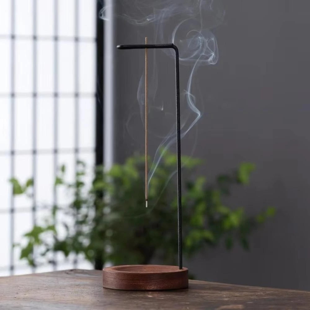 Minimalist wooden incense burner with a metal insert holding a lit incense stick, emitting smoke.