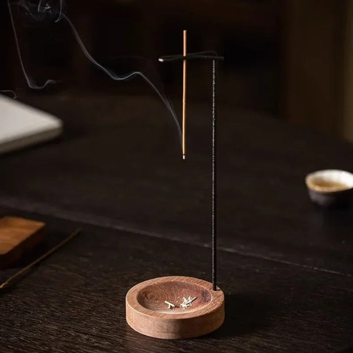 Minimalist wooden incense burner with a metal holder and a lit incense stick emitting smoke.