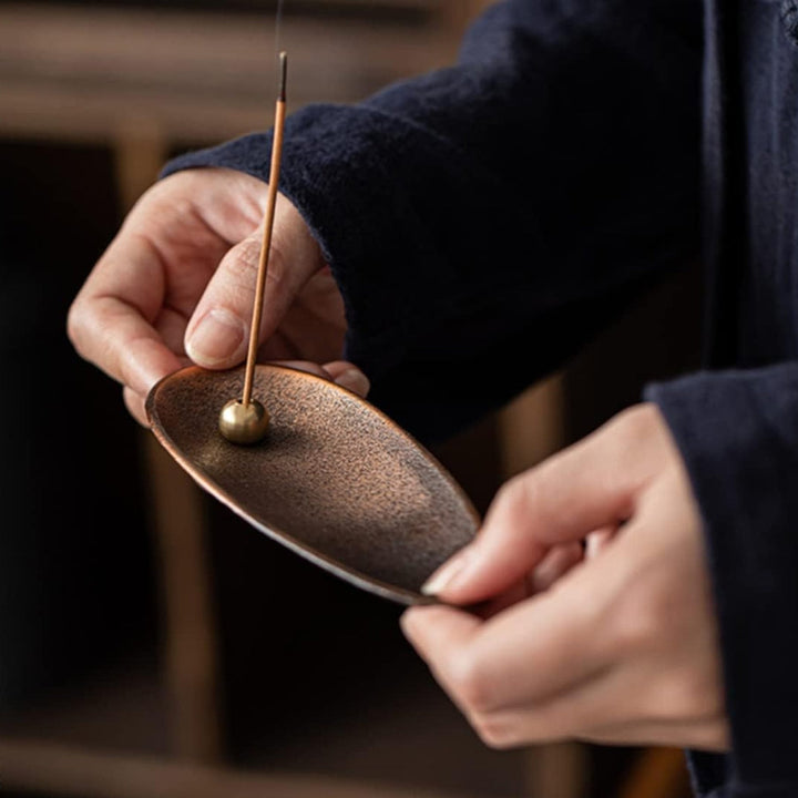 Hands holding a Zen Alloy Bead Incense Holder with an incense stick burning.