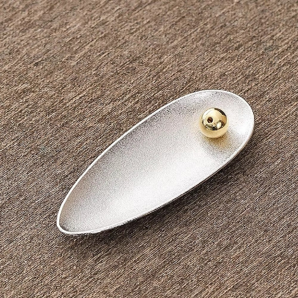 Silver oval incense holder with a gold bead that holds an incense stick at an adjustable angle.