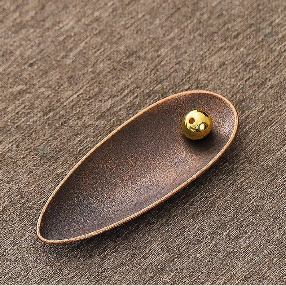 Bronze-colored, teardrop-shaped incense holder with a small, golden bead with two holes.