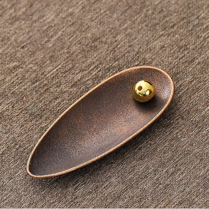 Bronze-colored, teardrop-shaped incense holder with a small, golden bead with two holes.