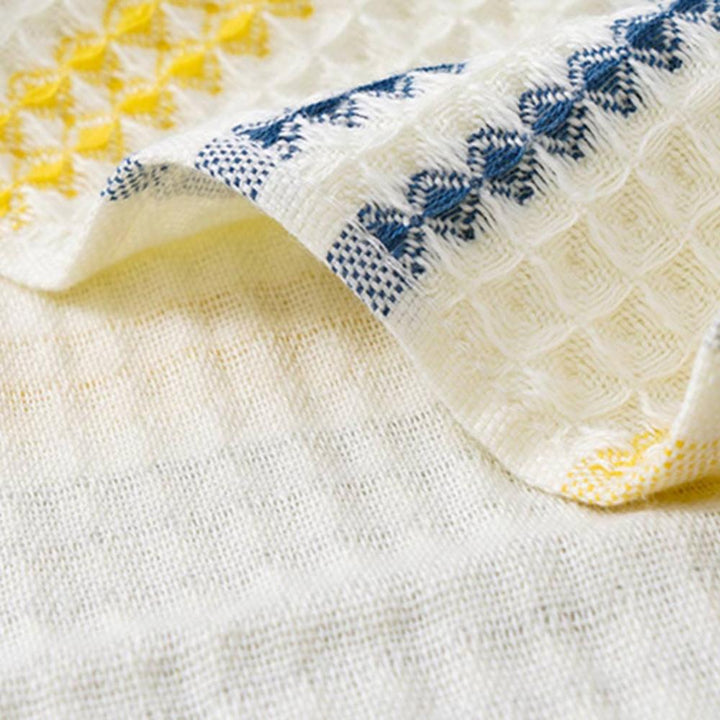Close-up of a white cotton bath towel with a honeycomb weave and blue and yellow embroidered stripes.