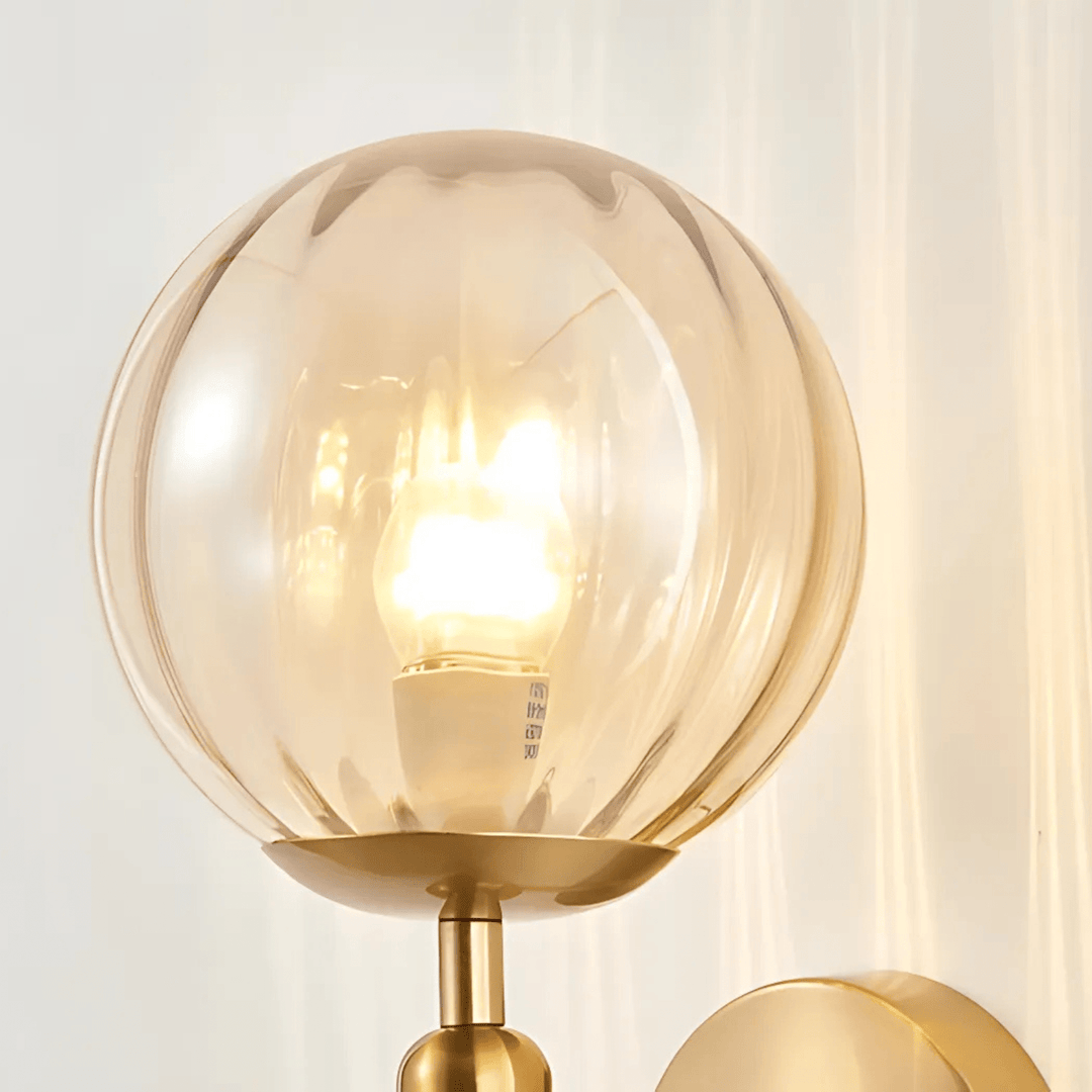Brass wall sconce with a round, fluted amber glass shade and a bright LED bulb inside.