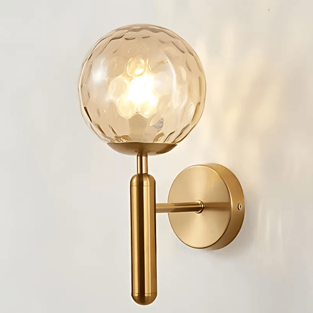 Brass wall sconce with a textured amber glass globe and a cylindrical brass arm.
