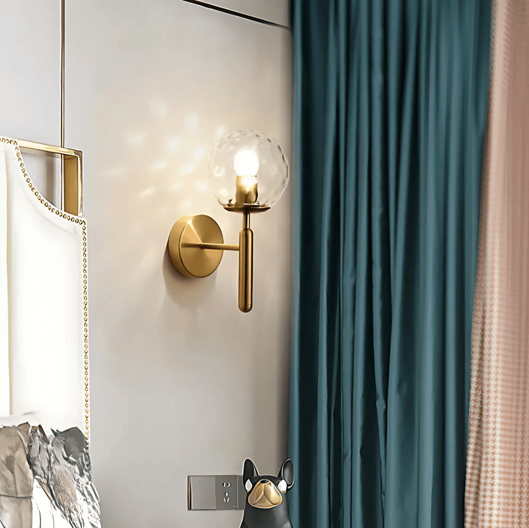 Brass wall sconce with a clear glass globe and a minimalist design, mounted on a light-colored wall.