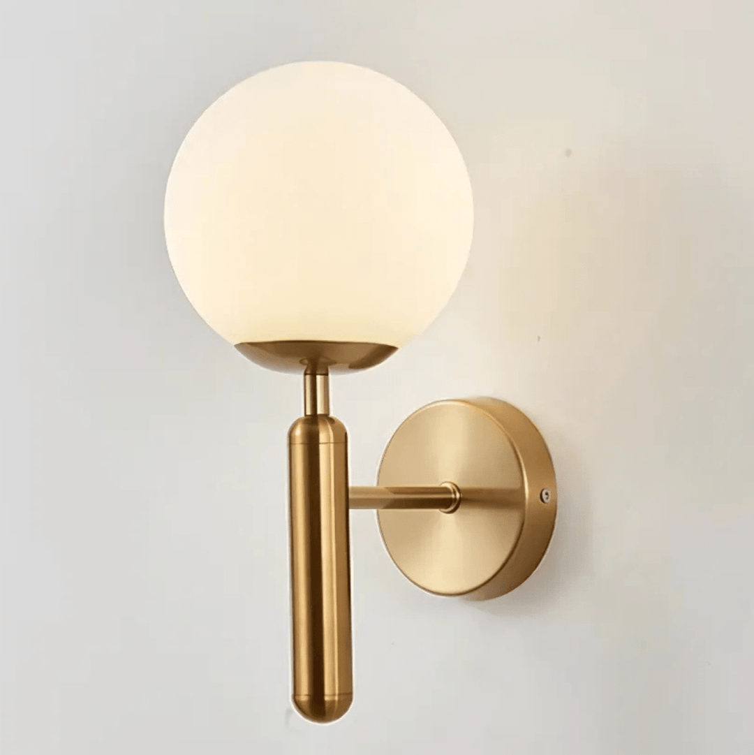 Brass wall sconce with a frosted globe light and a minimalist design.