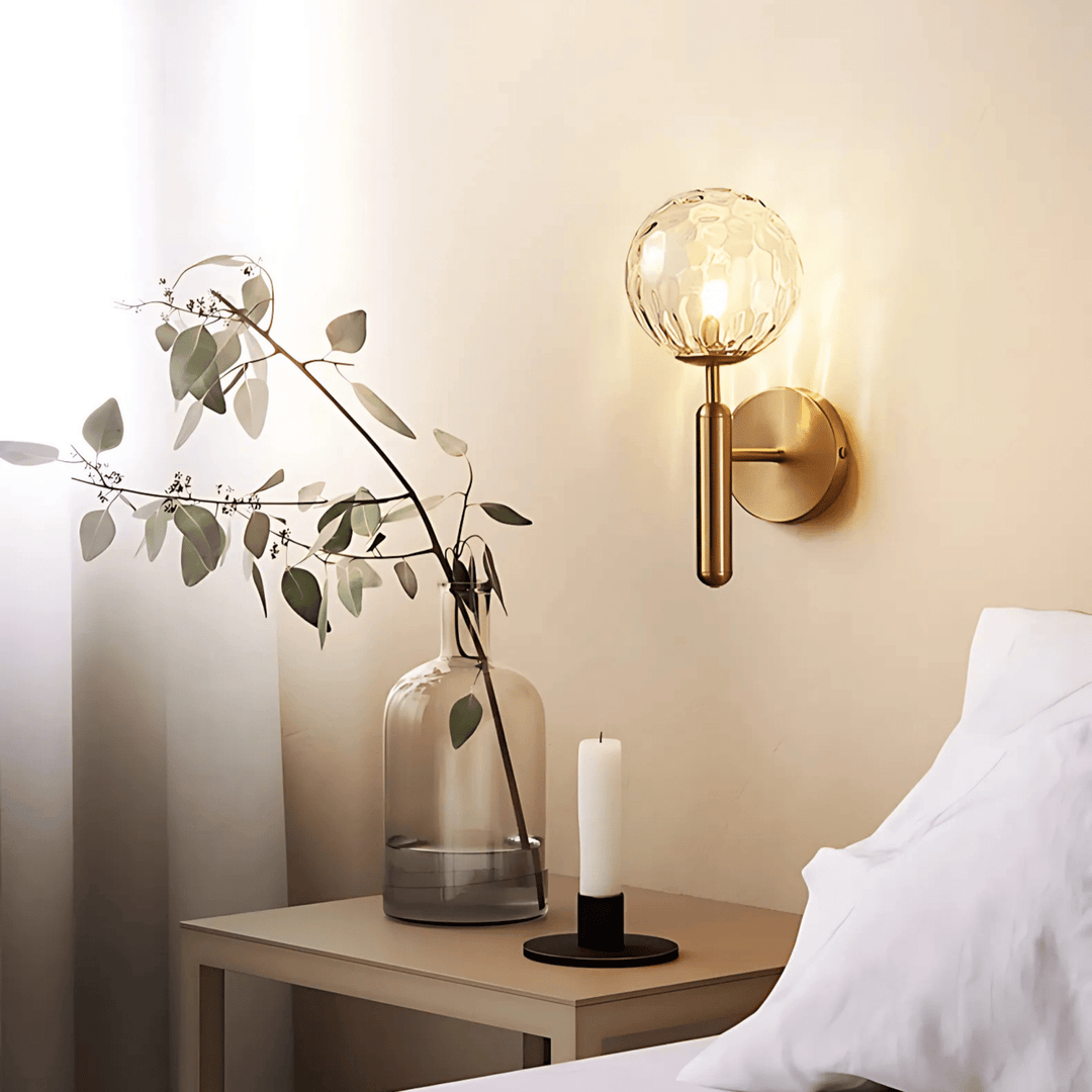 Brass wall sconce with a textured glass globe and a brushed brass finish, mounted on a wall above a nightstand.