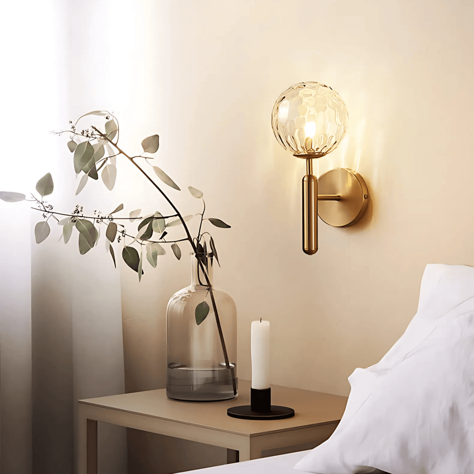 Brass wall sconce with a textured glass globe and a brushed brass finish, mounted on a wall above a nightstand.