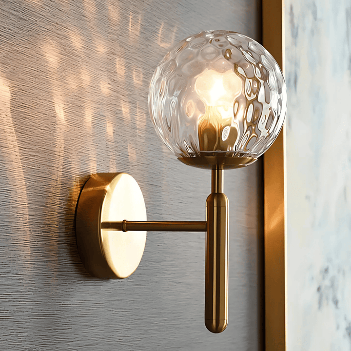 Brass wall sconce with a textured glass globe and a brushed brass finish, casting light patterns on the wall.