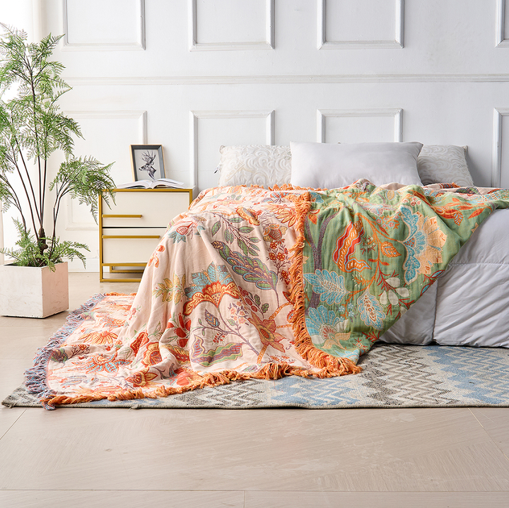 Rustic floral boho cotton blanket draped on a bed, featuring a peach and green side with tassels.