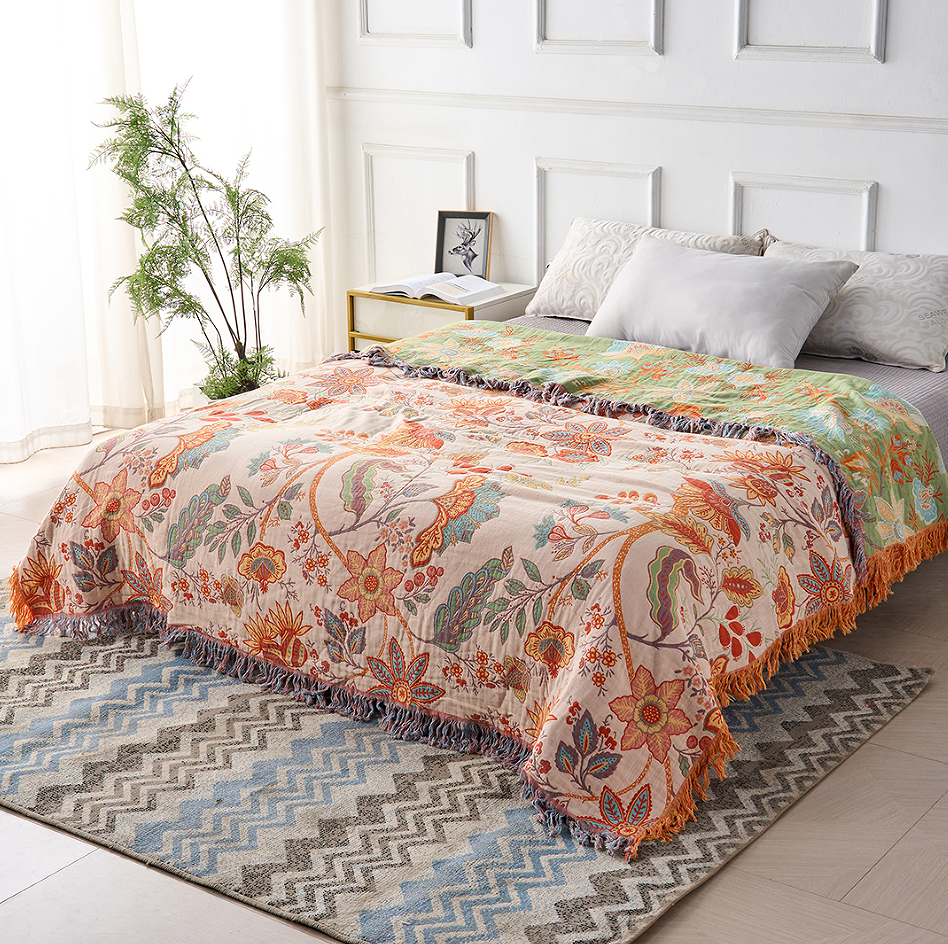 Rustic floral boho cotton blanket with tassels draped on a bed with pillows and a rug.