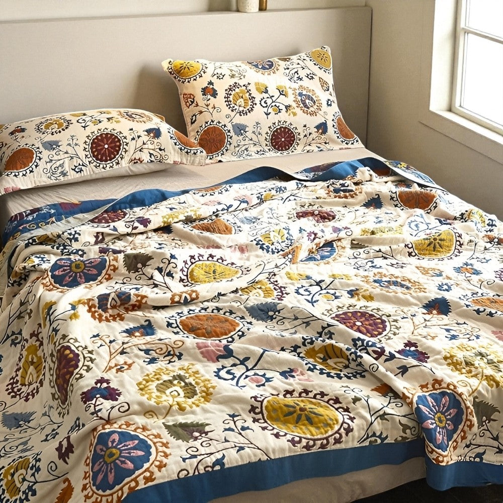 Breathable cotton gauze coverlet with a colorful floral pattern and a blue trim, shown on a bed with two pillows.