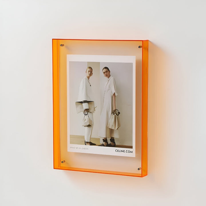 Orange acrylic picture frame displaying a fashion ad with two models and "CELINE.COM" text.