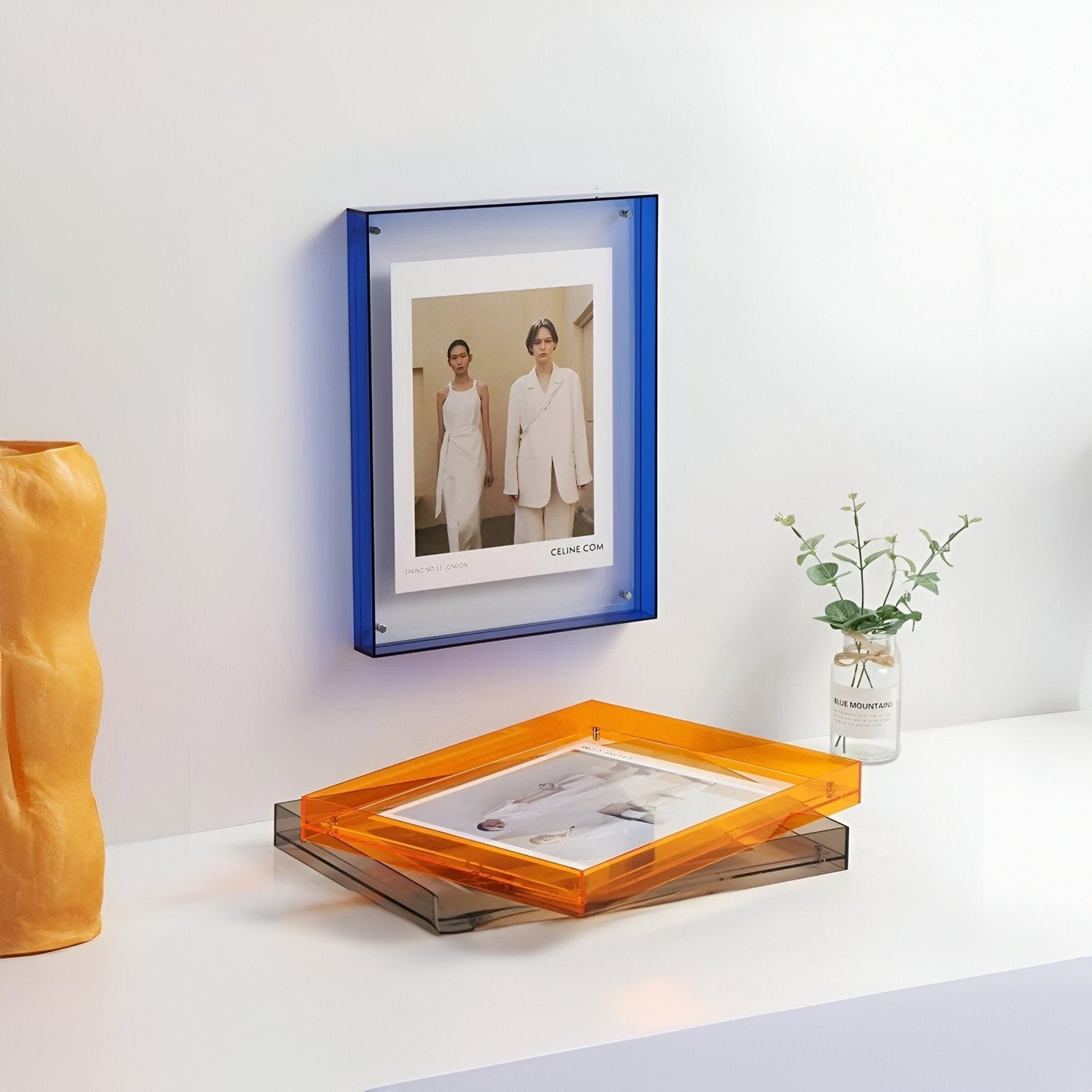 Blue and orange acrylic picture frames displaying fashion photos on a white surface.