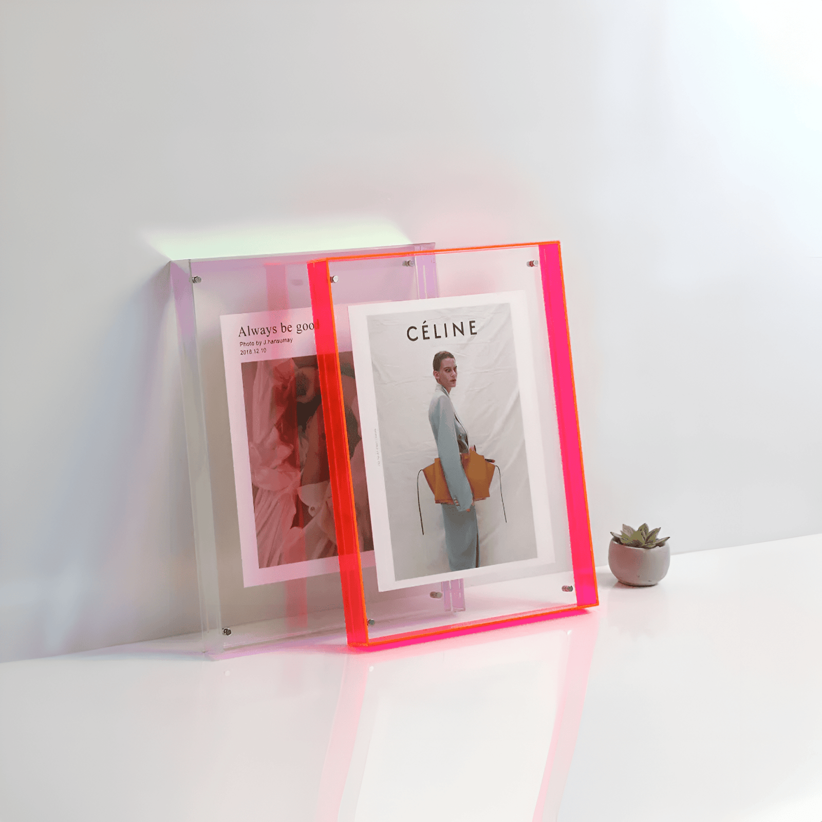Two acrylic picture frames, one with a pink gradient and the other with a neon pink border, display magazine pages.