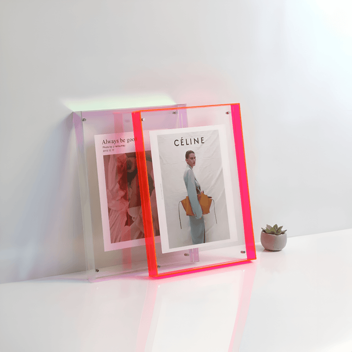 Two acrylic picture frames, one with a pink gradient and the other with a neon pink border, display magazine pages.