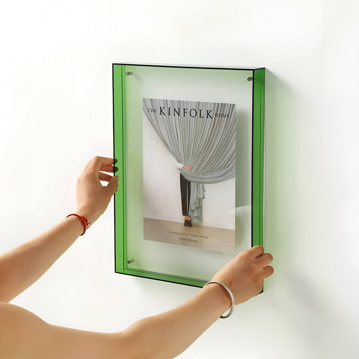 A person holds a modern, transparent green acrylic picture frame against a white wall.
