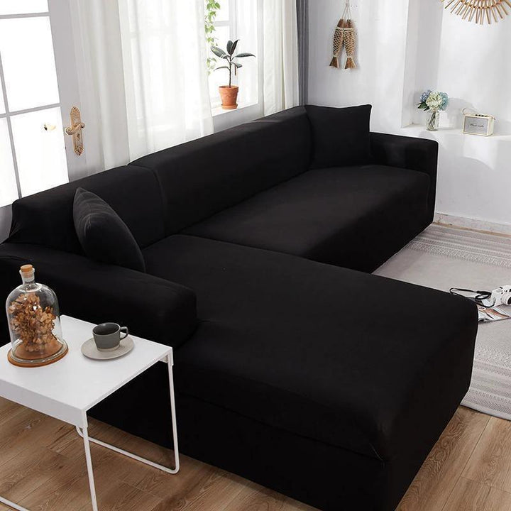 Black L-shaped sofa cover on a sectional sofa, with a small white table and a glass dome with dried flowers in front.