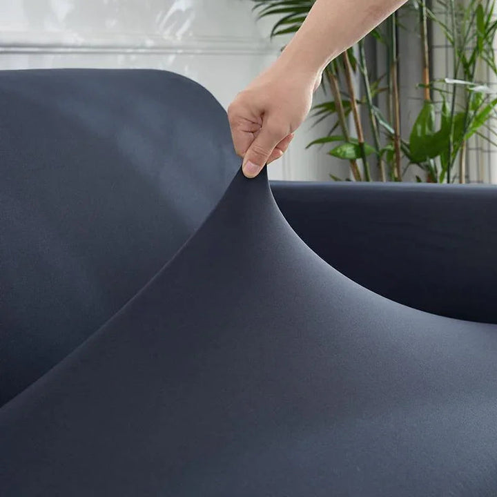 Hand stretching a dark grey, soft fabric sofa cover over a couch.